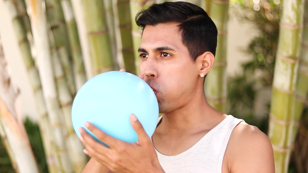 retrato de un joven latino inflando un globo de látex