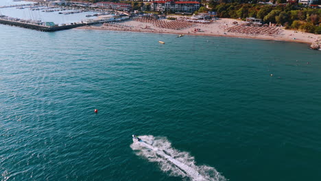 following a jet ski scooter riding by the turquoise waterscape along the beautiful beach. yacht club with multiple vehicles at backdrop. sveti vlas, bulgaria