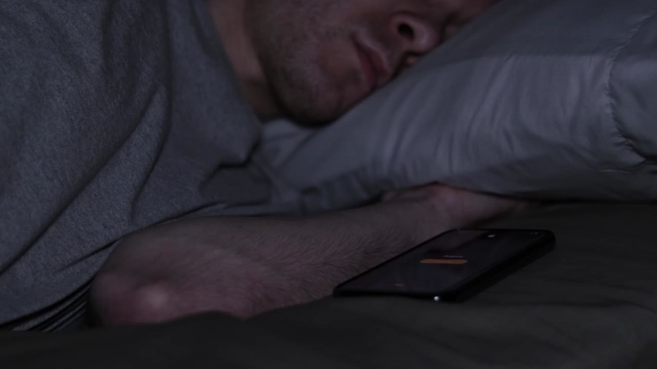 hombre despertándose en la cama con la alarma de su teléfono inteligente