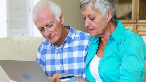 pareja de ancianos comprando en línea usando computadora portátil con tarjeta de crédito en la sala de estar