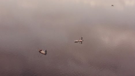 Toma-Aérea-Girando-Alrededor-De-Dos-Trabajadores-De-Extracción-De-Sal-En-El-Lago-Dakar,-Con-Las-Nubes-Reflejadas-En-Su-Superficie