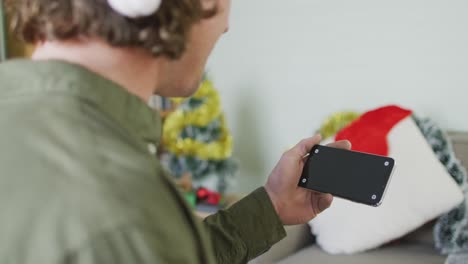 Feliz-Hombre-Caucásico-Con-Sombrero-De-Papá-Noel-Usando-Un-Teléfono-Inteligente-En-Navidad