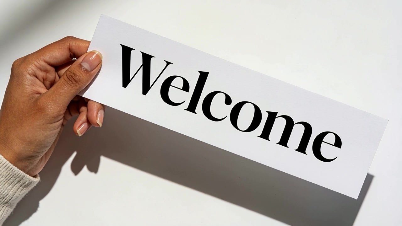 Entering left hand holding Welcome card, adjusting card on tabletop with cream cuff to show Welcome