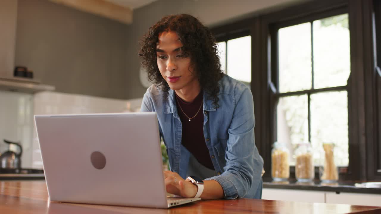 Entering kitchen, non-binary person placing laptop on wooden island and typing for remote work