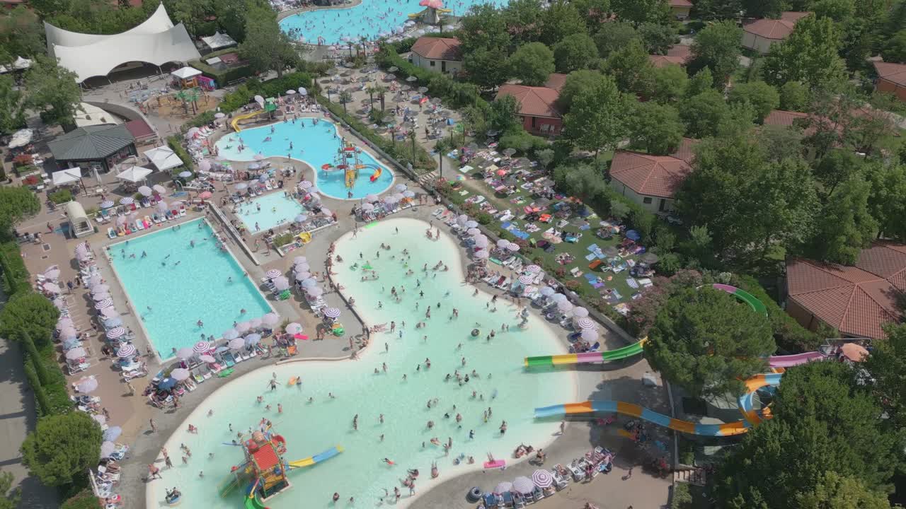 Drone orbits bird's eye view perspective above busy swimming pool with tourists
