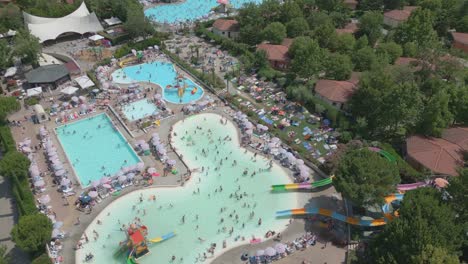 Drone-orbits-bird's-eye-view-perspective-above-busy-swimming-pool-with-tourists