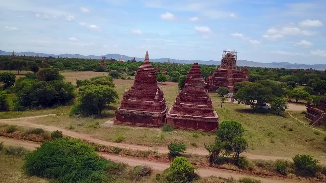 A stunning pull-out drone shot showcasing the First Temple in Bagan, Myanmar, crafted from red brick and surrounded by lush green landscapes. A striking view of history and nature.