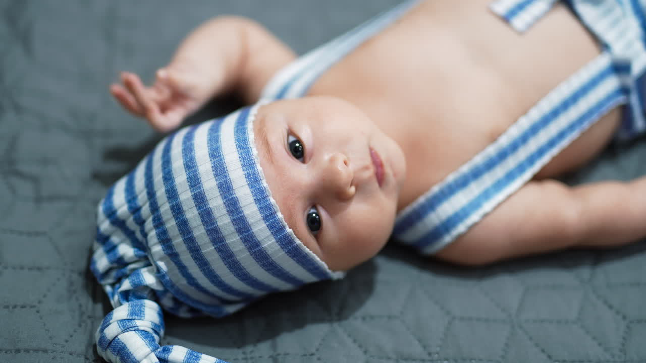 Toddler in a funny blue and white suit on the bed. Baby lies on the bed with his head to the camera. Close up.