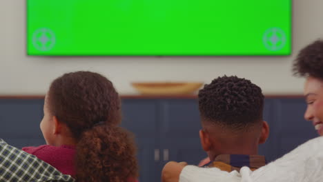 camera pans along rear view of family sitting on sofa at home watching green screen tv and laughing at comedy - shot in slow motion
