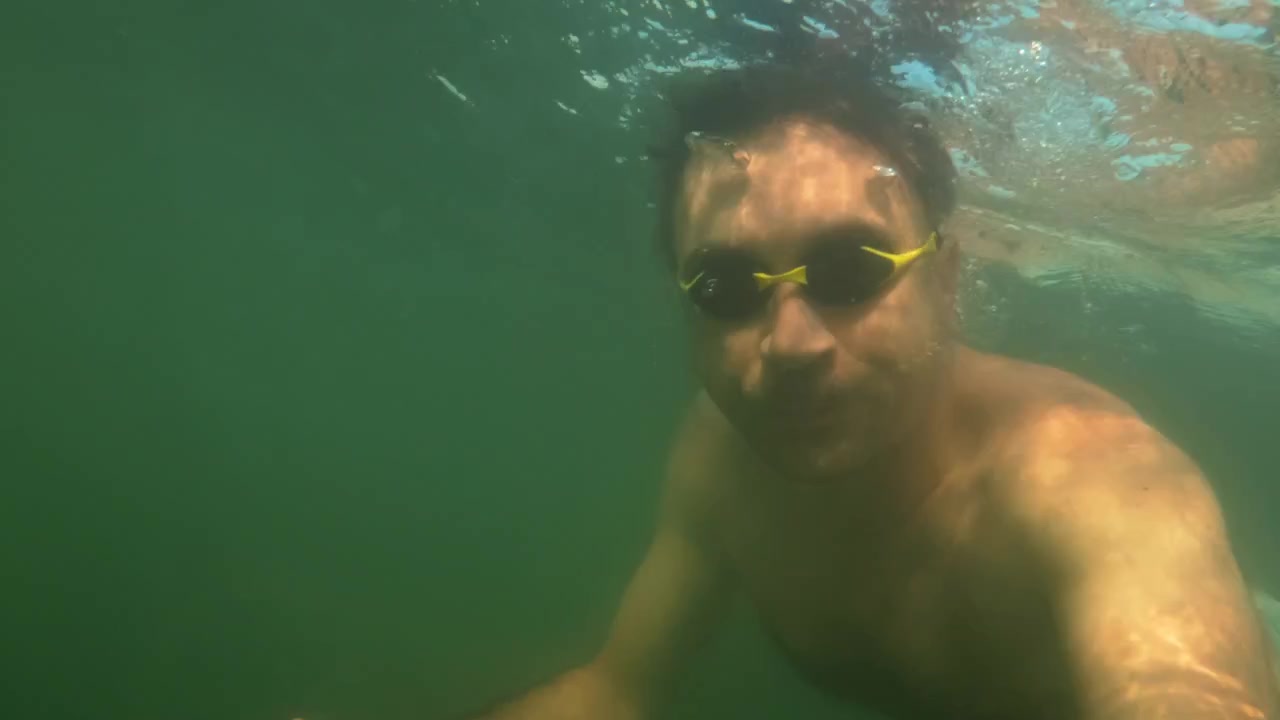 Hombre nadando bajo el agua en agua verde clara, creando una masa de burbujas cerca de la superficie, con luz cálida reflejándose.