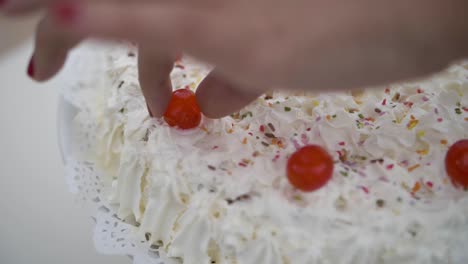 mano caucásica poniendo caramelo de cereza roja en pastel de crema blanca con chispas de colores en el evento de celebración familiar