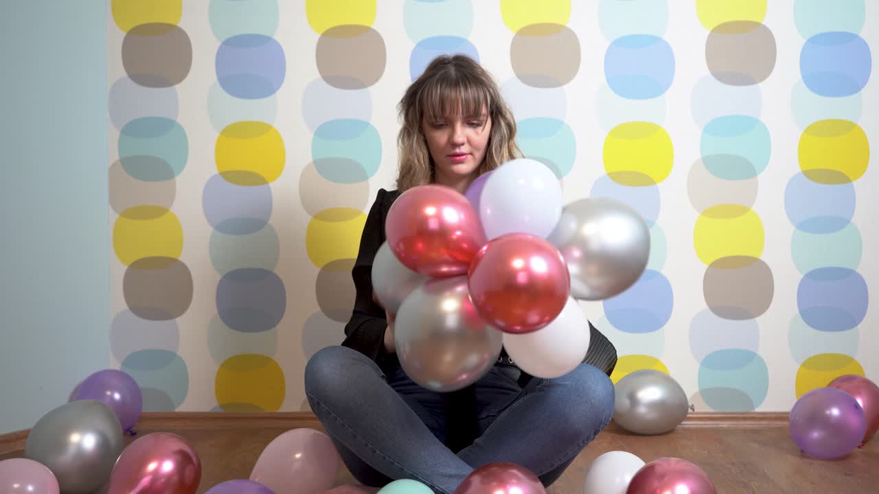 mujer joven sentada alrededor de globos y jugando con globos contra un fondo colorido