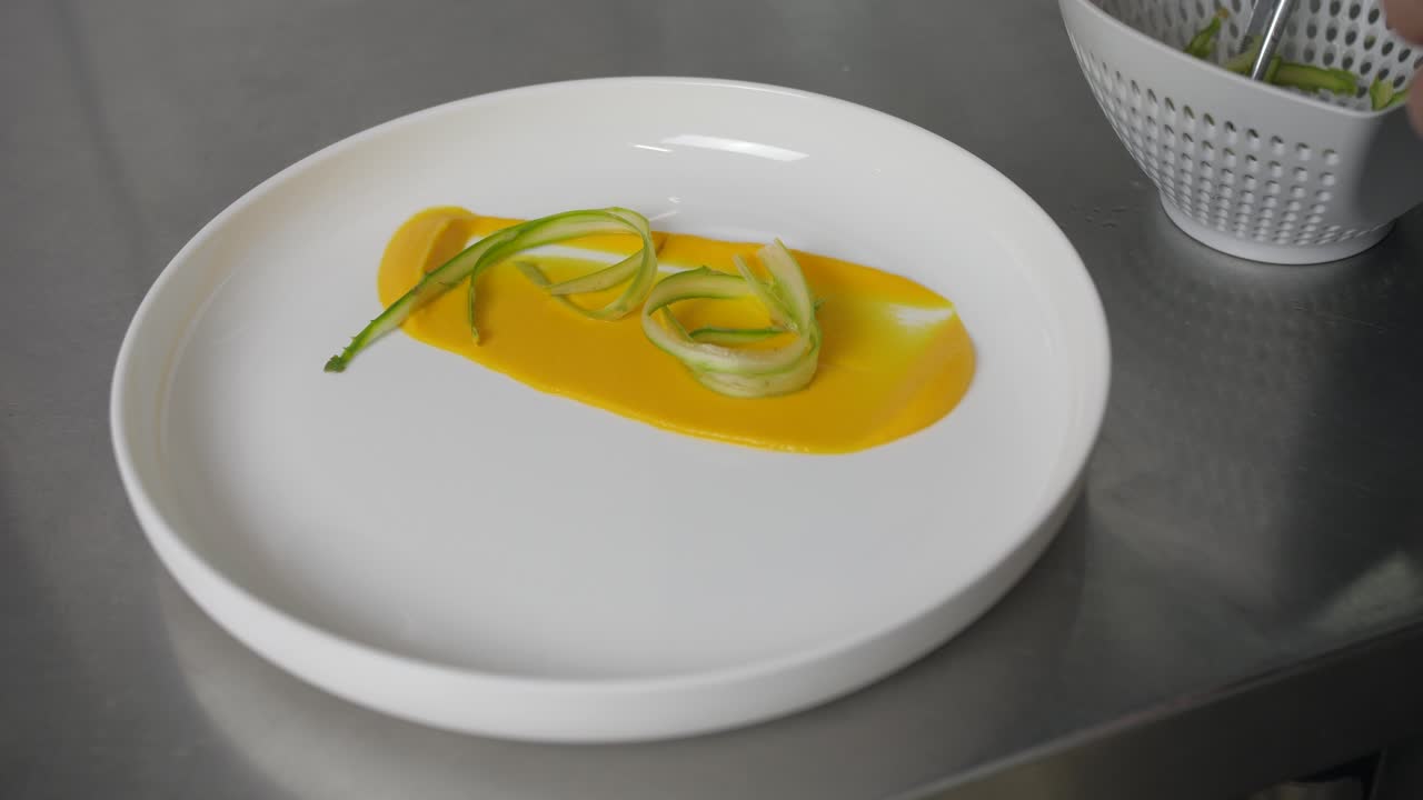 lo chef decora con cura la purea gialla sul piatto bianco con verdure verdi