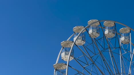 low angle shot of slowly rotating ferris wheel against blue sky in sunlight,4k