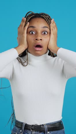shocked young woman with hands on face against blue background