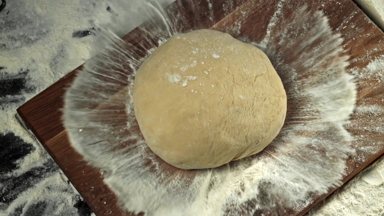 Palla di impasto che cade su un tagliere di legno infarinato al rallentatore.