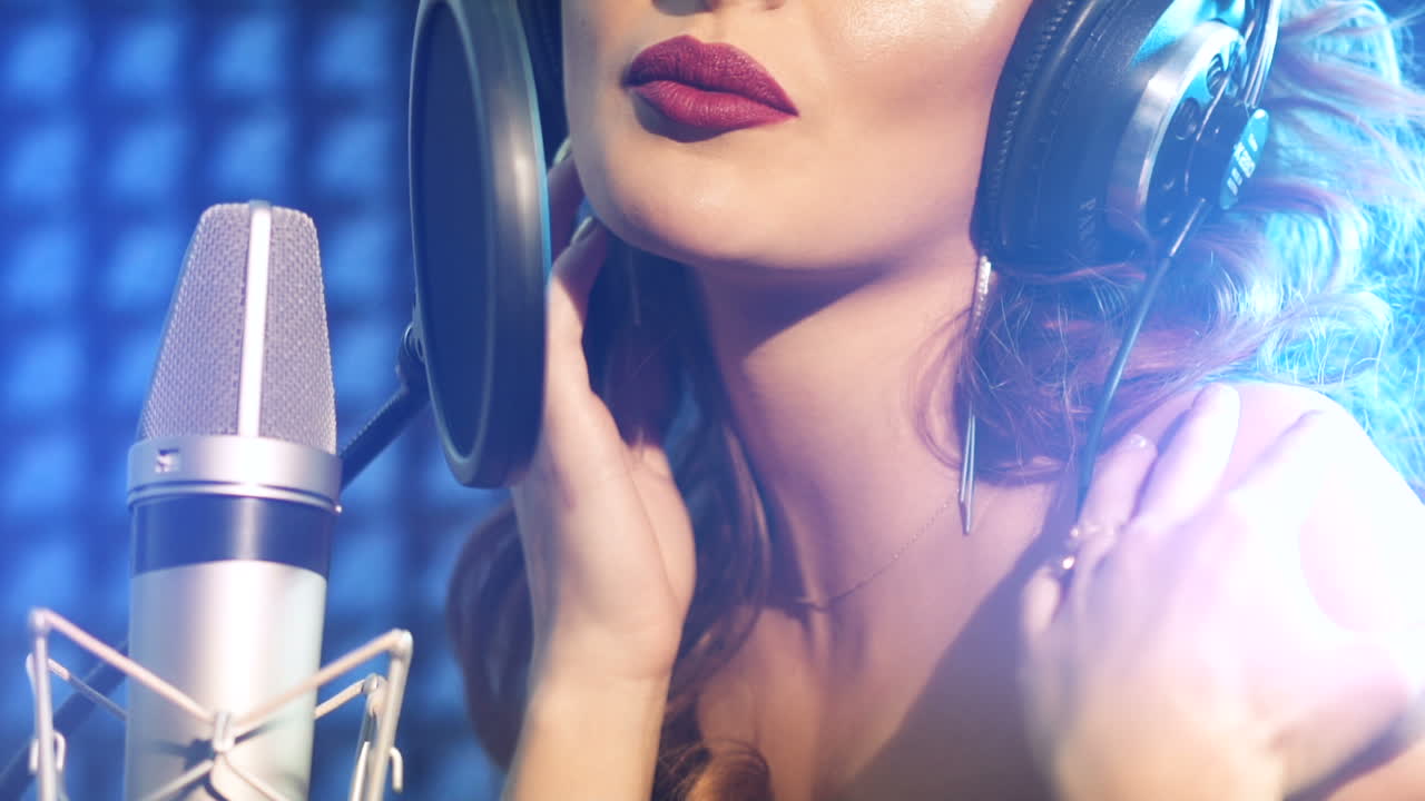 Young woman recording a song in a professional studio. Close-up face. Slow motion