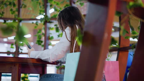 woman seated in a well-decorated bar, deeply focused on her phone, with a lively atmosphere and vibrant decor creating an inviting backdrop