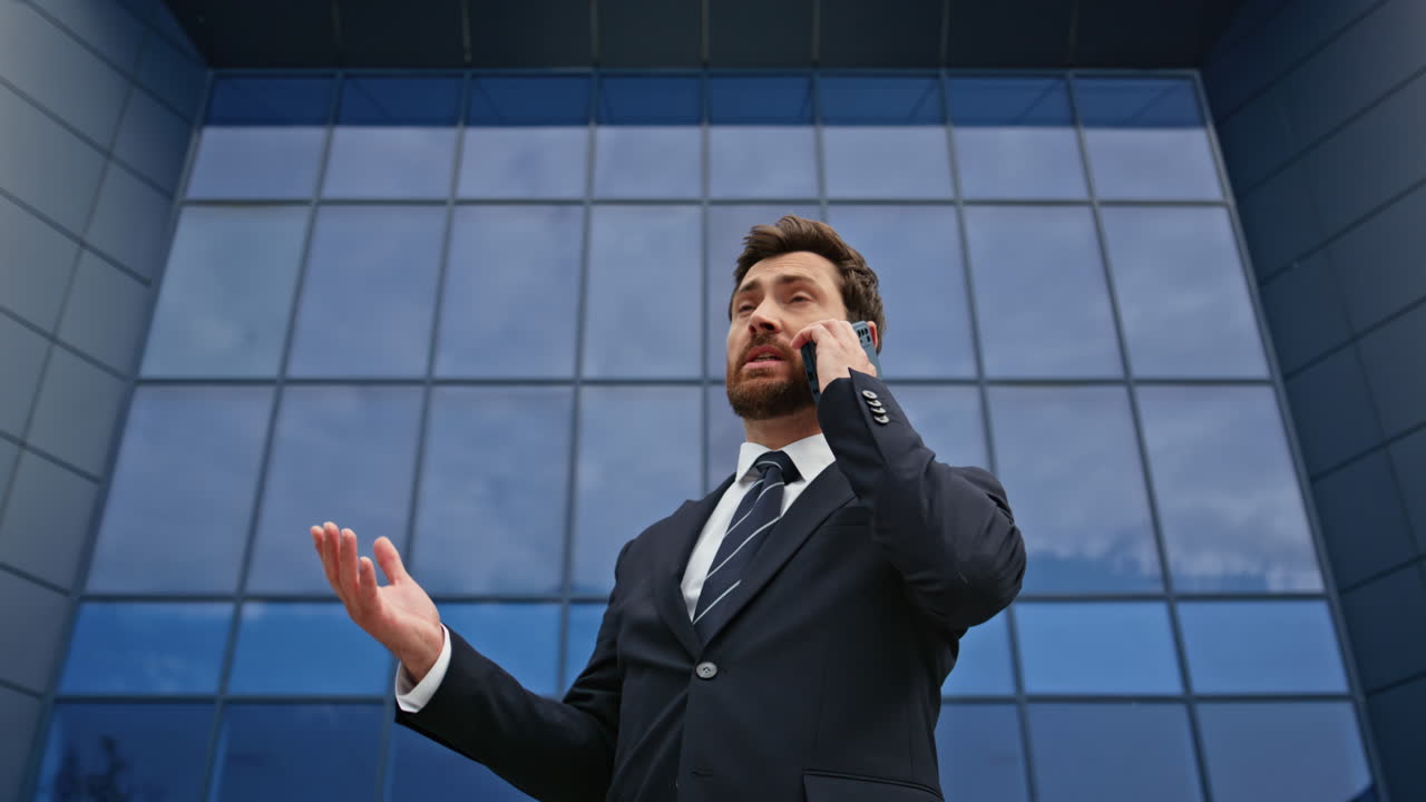 Executivo irritado discutindo ao celular gesticulando expressivamente perto do escritório em close-up