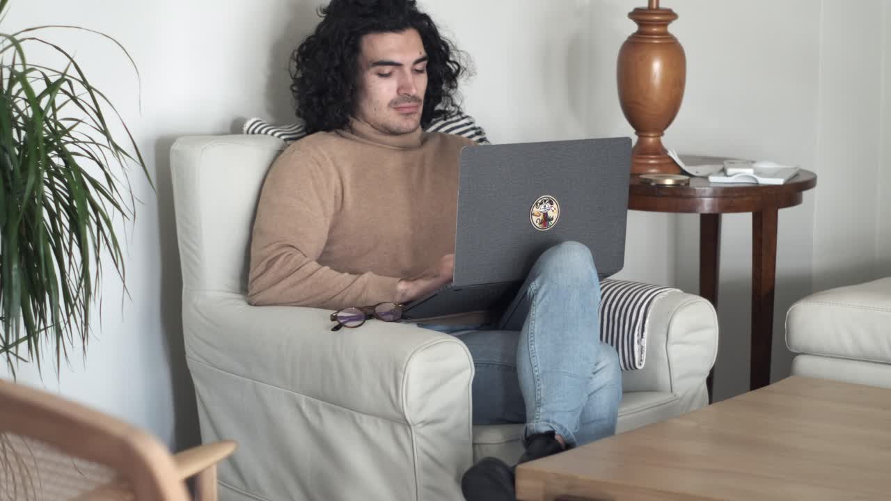 Remote Work Routine: Caucasian Young Man with Long Curly Hair Gets Productive on Sofa