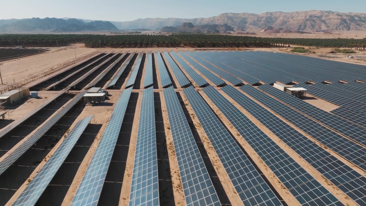 Højkvalitets luftdroneoptagelse, der flyver over omfattende rækker af fotovoltaiske solpaneler, der genererer vedvarende ren energi i et tørt ørkenlandskab.