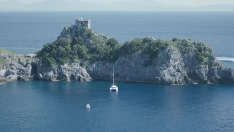 catamaran sailboat and small boats docked near rocky headland with torre del capo di conca atop on the amalfi coast in italy