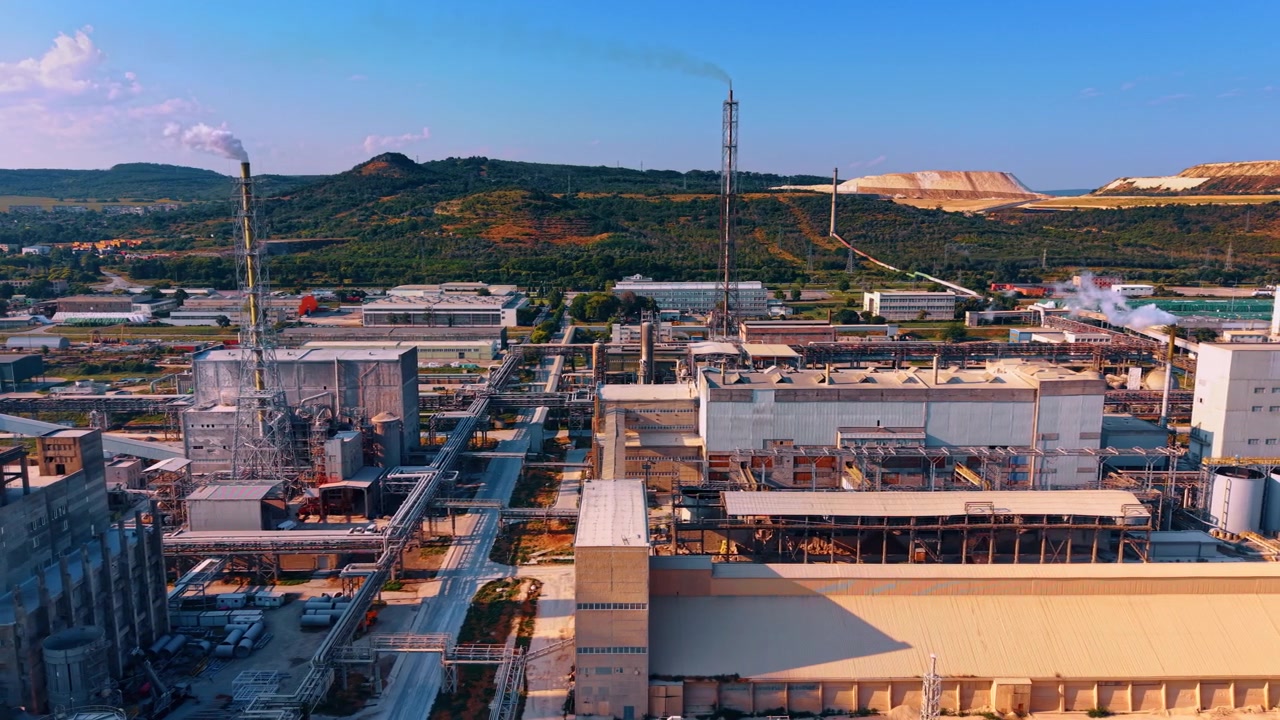 Complejo de fábrica con altas chimeneas de acero y redes de tuberías. La luz del día ilumina las extensas estructuras industriales situadas contra colinas verdes