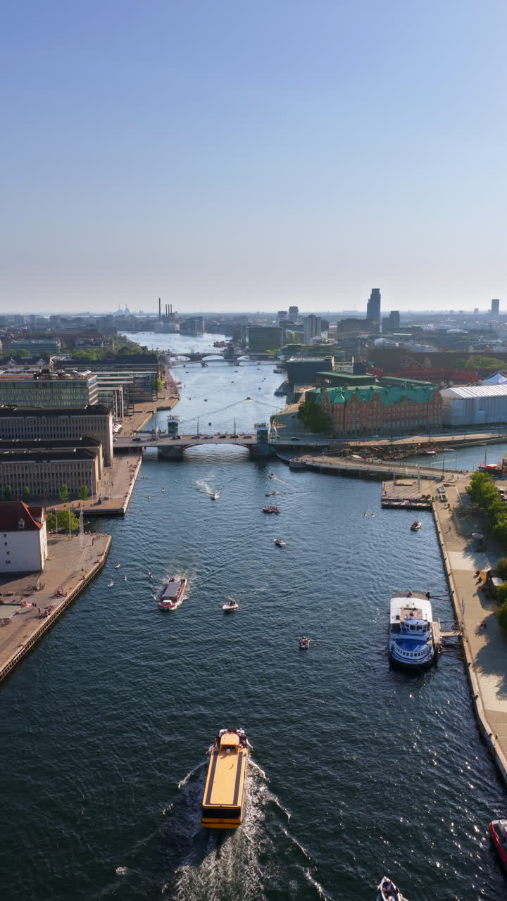 Aerial drone view of Copenhagen's harbor, featuring canals, bridges, and boats, with the yellow harbor bus cruising through the water. Vertical