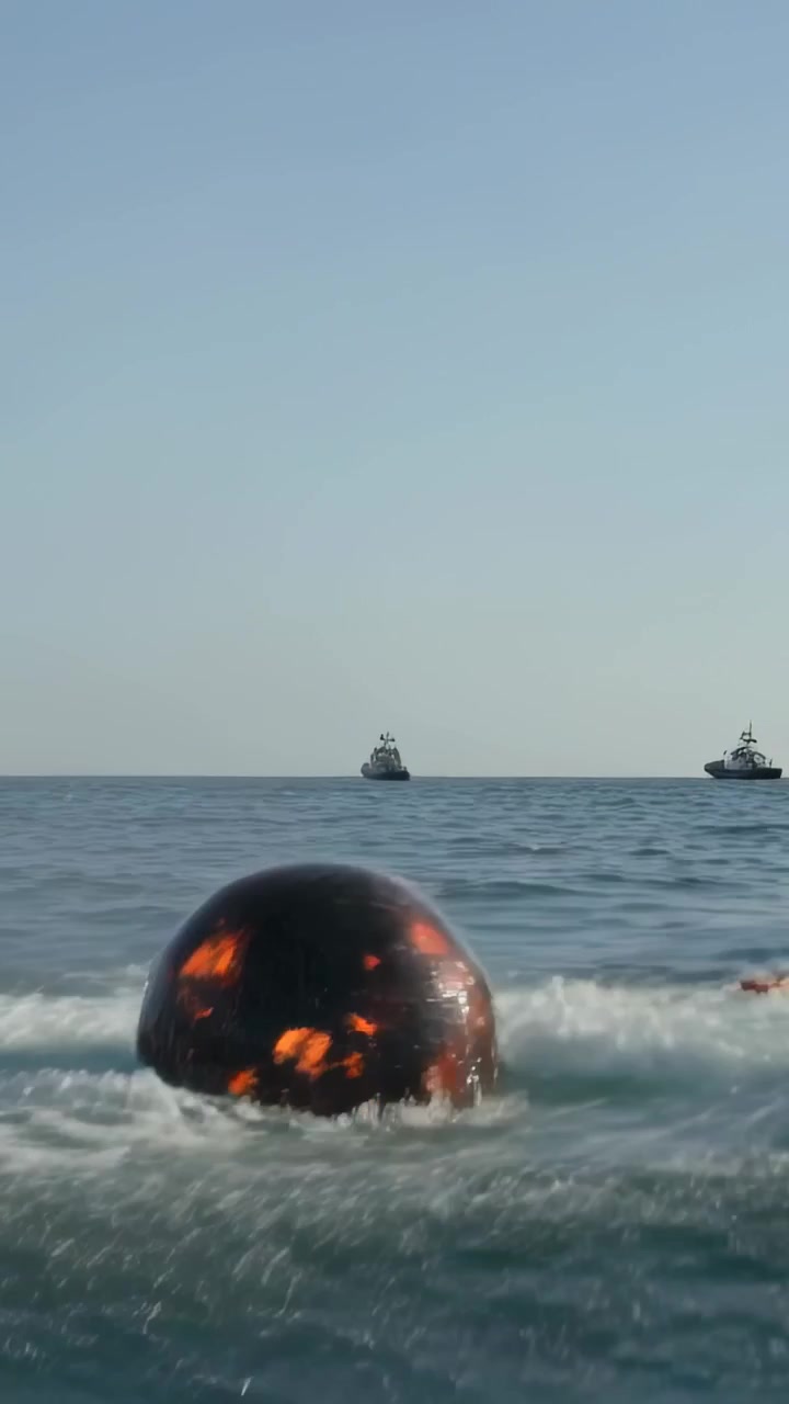 Dikey video: Denizde bir patlamadan sonra yüzeye çıkan parlayan küre, çekme kayışı ile uzaklaştırılıyor, metin alanı.