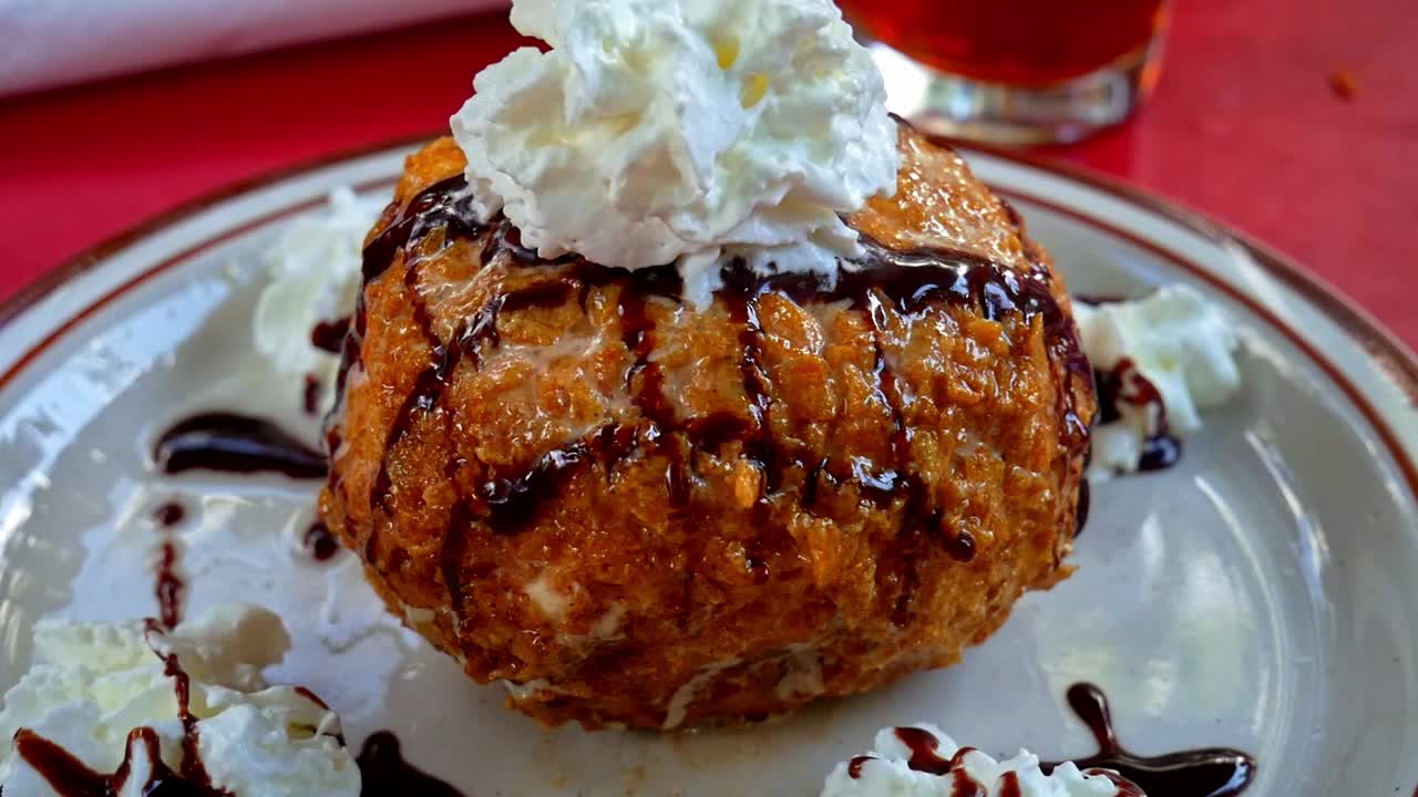 Fried ice cream dessert with whipped cream and chocolate sauce on a white plate