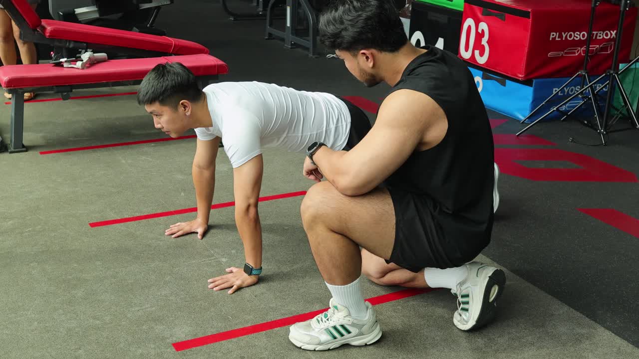 A personal trainer assists a client performing mountain climbers in a gym setting, emphasizing technique and motivation