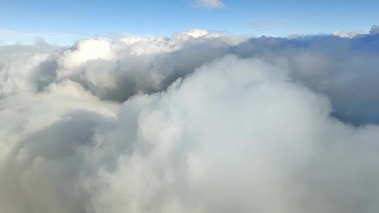 Calm flight through sunny blue sky with large fluffy clouds passing peacefully. View from cruising altitude