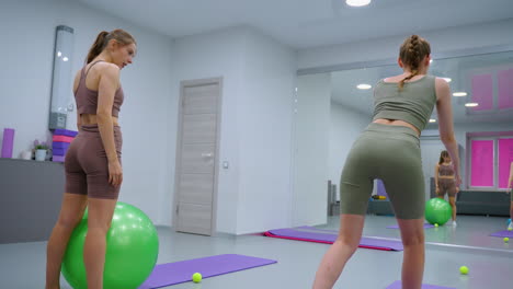 vista trasera de una sesión de ejercicio de fitness mientras un instructor observa a un aprendiz estirándose hacia adelante, preparándose para ayudar a corregir la postura, con un gran espejo que refleja la escena en un gimnasio moderno