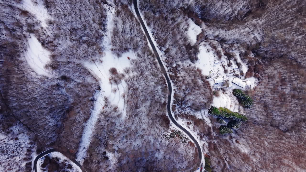 Vista aerea innevata di strada tortuosa attraverso un paesaggio forestale invernale