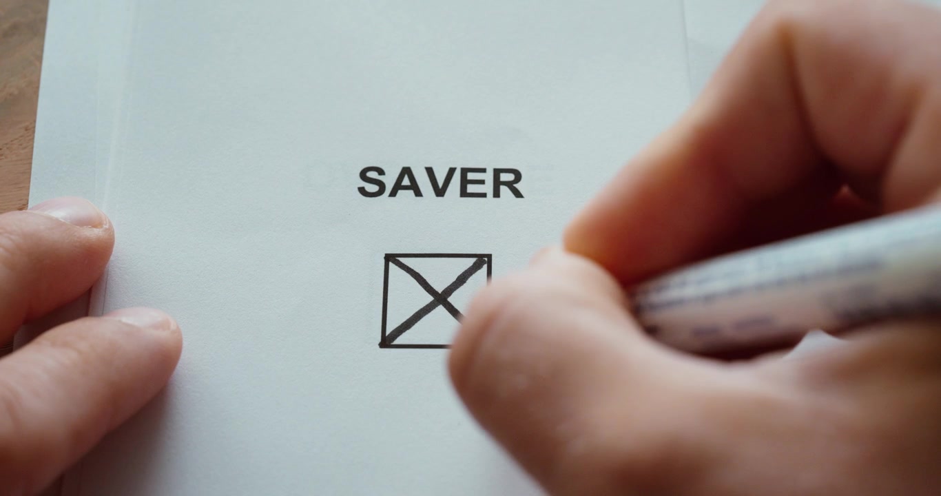 Close-up of a person using a black marker to check a checkbox labeled Saver on a printed paper. Concept of saving money, personal finance, budgeting, financial planning and responsible spending.