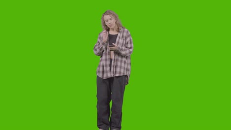 full length studio shot of young woman listening to music on mobile phone and dancing against green screen