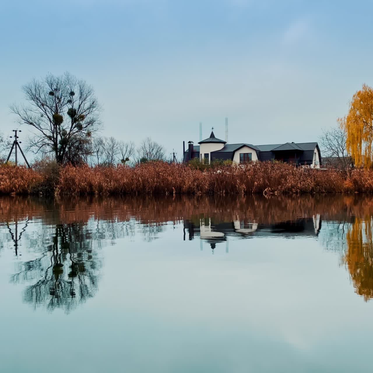 Beautiful modernly-designed cottage house built on the bank of river. Colorful trees growing on the waterfront. Blue skies backdrop