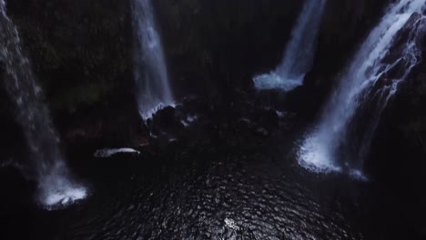 drone shot lowering down and panning up revealing four gushing waterfalls pouring into a large swimming hole