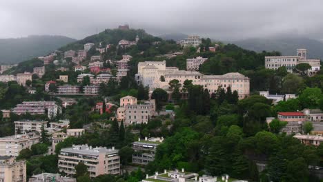 hillside full of buildings with green vibrant trees on moody stormy day, aerial cinematic view