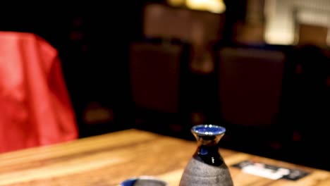 a hand grasps a frothy beer mug beside a traditional sake bottle on a wooden table.