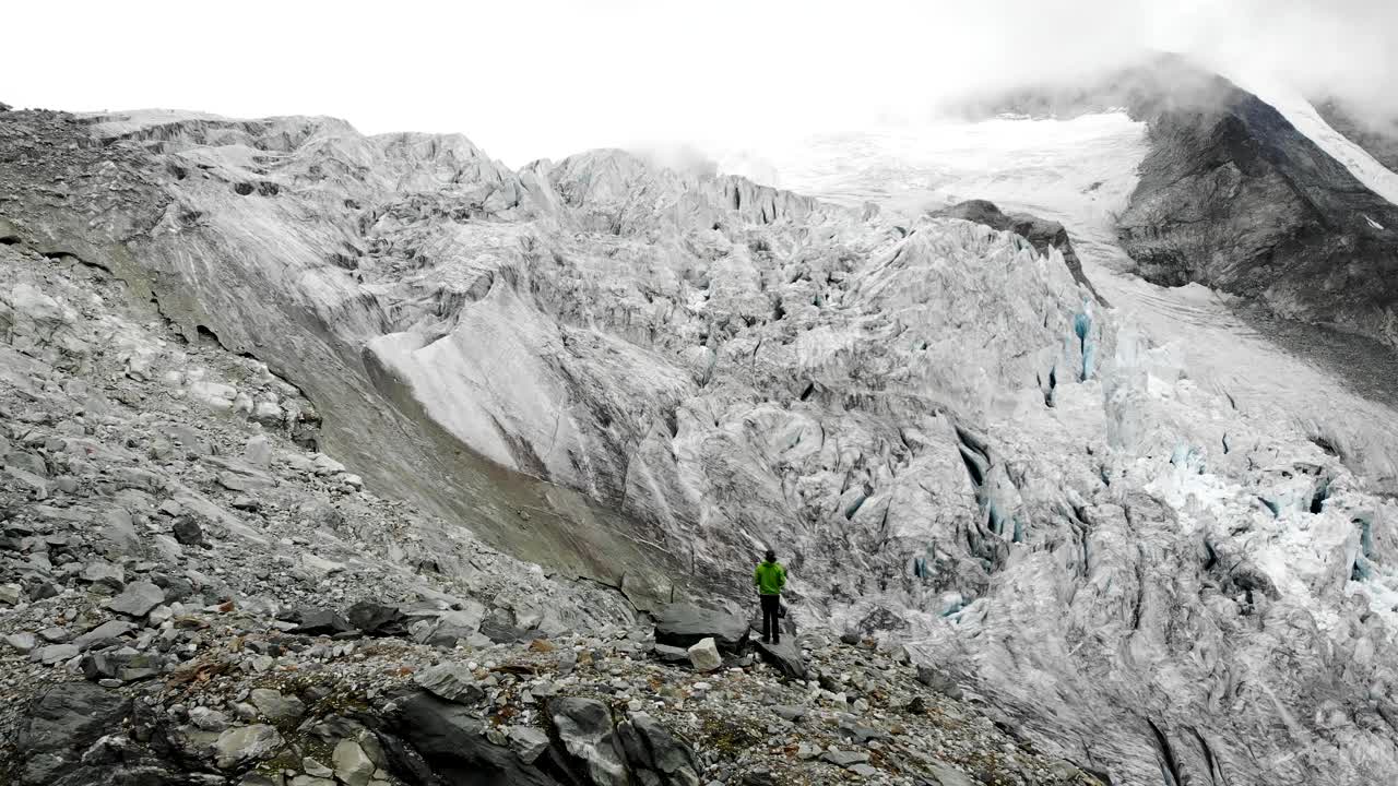 sobrevuelo aéreo sobre un excursionista hacia el borde del glaciar moiry cerca de grimenz en valais, suiza, con vistas a las grietas heladas y los picos alpinos escondidos en las nubes