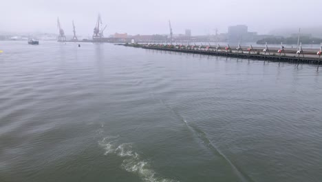 boat cruising in gota alv, gothenburg with container cranes in the misty background - high angle shot