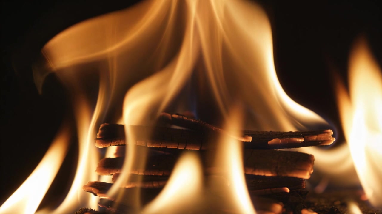 Flakkende flammetunger antænder en stak tynde træpinde på en mørk baggrund, der danner gløder.
