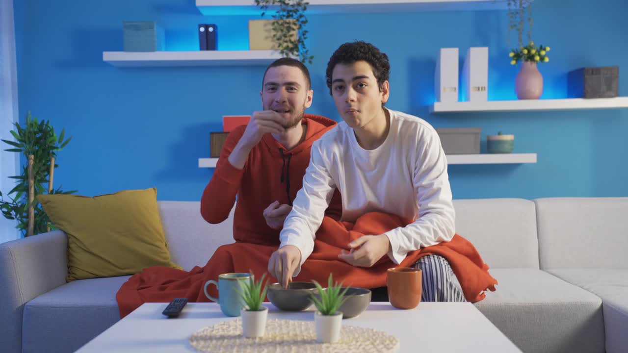 Younger brother and younger brother are watching movie on TV while relaxing on sofa at home.