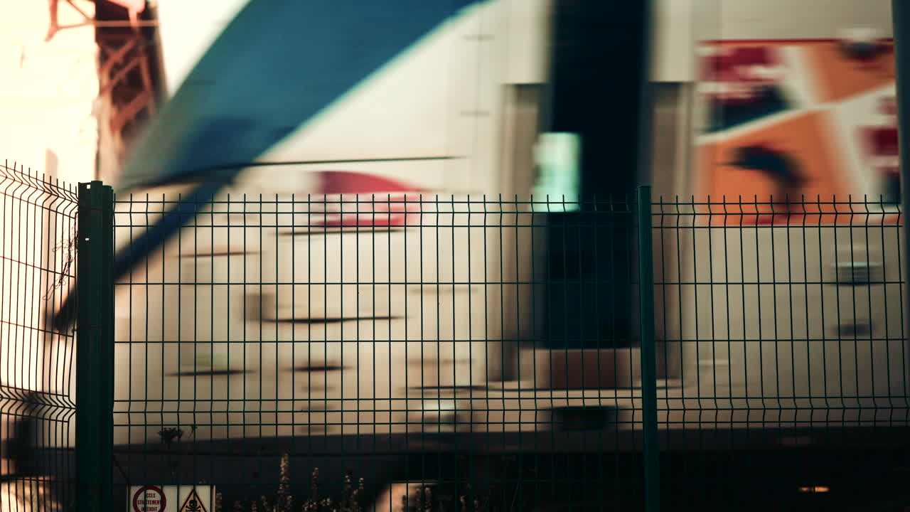 Blurred train passing behind a metal fence, creating an abstract transportation scene with strong graphic lines