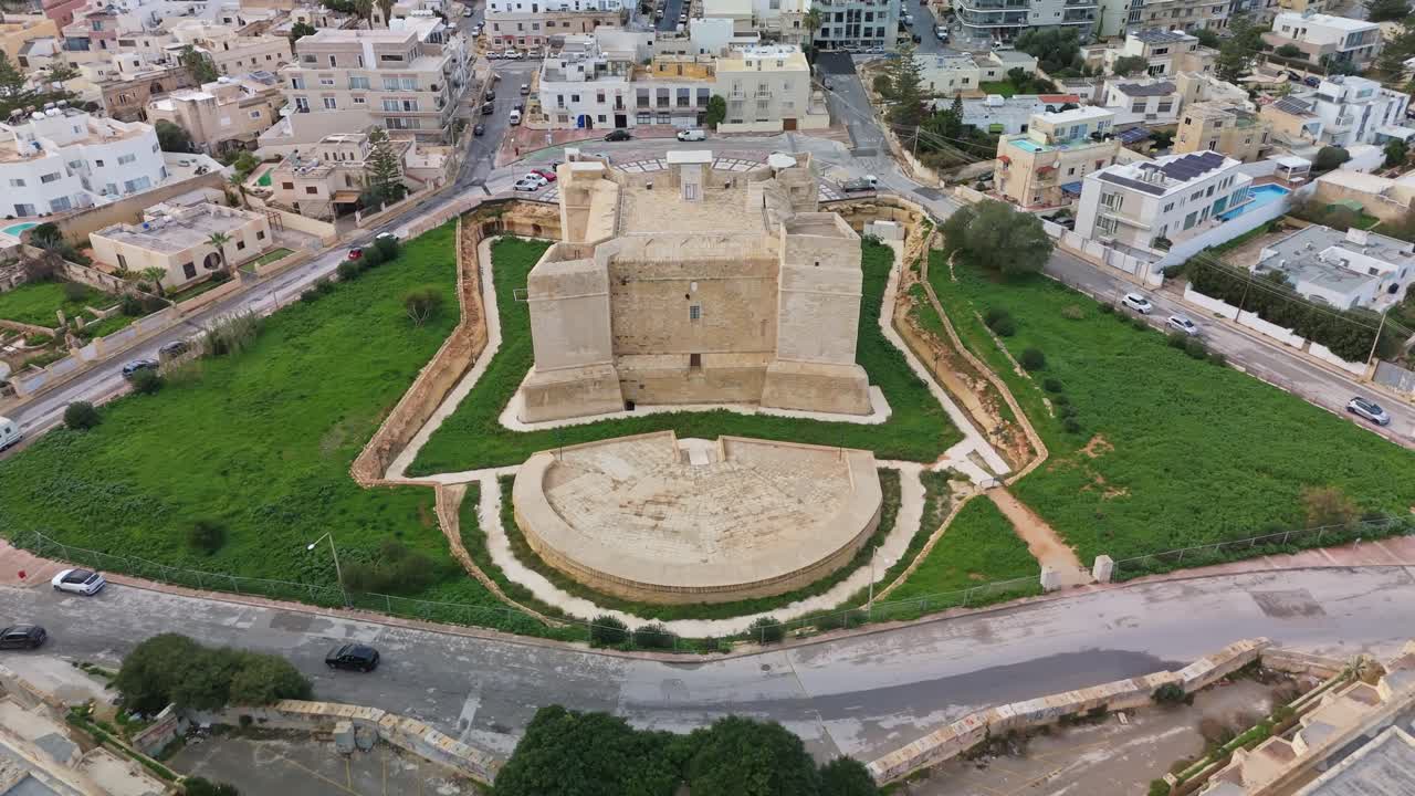Ripresa aerea ascendente della torre di San Tommaso, una torre di avvistamento medievale in pietra calcarea a Marsaskala, Malta, circondata da paesaggi urbani, che ne mette in mostra il significato storico e il fascino mediterraneo