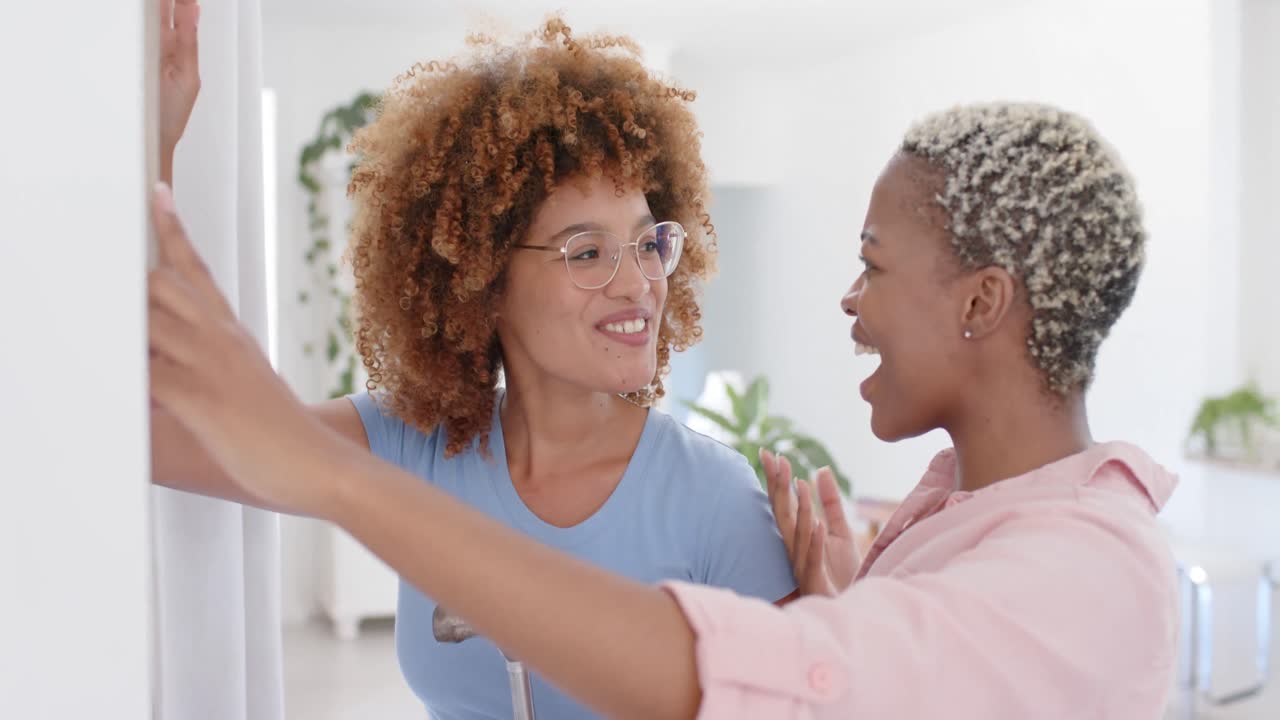 Happy diverse female couple taking notes on wall in slow motion