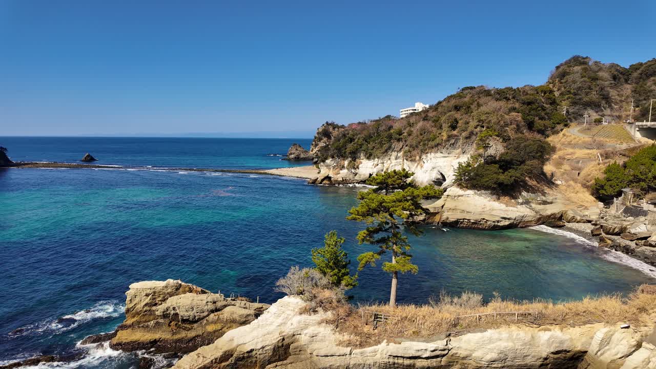Una panoramica ampia e mozzafiato di una splendida baia giapponese, caratterizzata da acque turchesi vibranti, scogliere rocciose bianche e un hotel resort costiero annidato lungo la costa frastagliata della penisola di Izu.