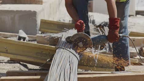 a construction worker wearing red gloves is cutting steel rebars using an angle grinder, producing a bright shower of sparks. the scene highlights the precision and skill needed in construction work