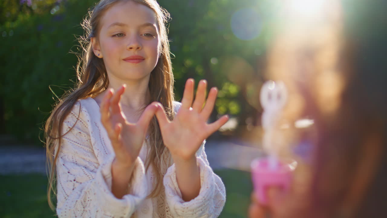 Relaxing kid playing soap bubbles with mom on sunny day in weekend park closeup